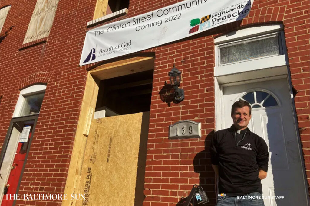 Rev. Mark Parker, pastor of Breath of God Lutheran Church in Highlandtown, stands by two burned-out rowhouses being converted into a child care center and housing for refugees.